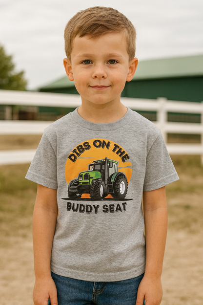 Child wearing a gray t-shirt with a tractor graphic and text in an outdoor setting.