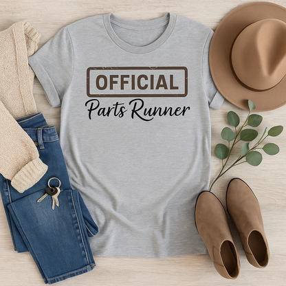 Gray t-shirt with 'OFFICIAL Parts Runner' text, paired with jeans, a hat, boots, and a sweater on a wooden surface.