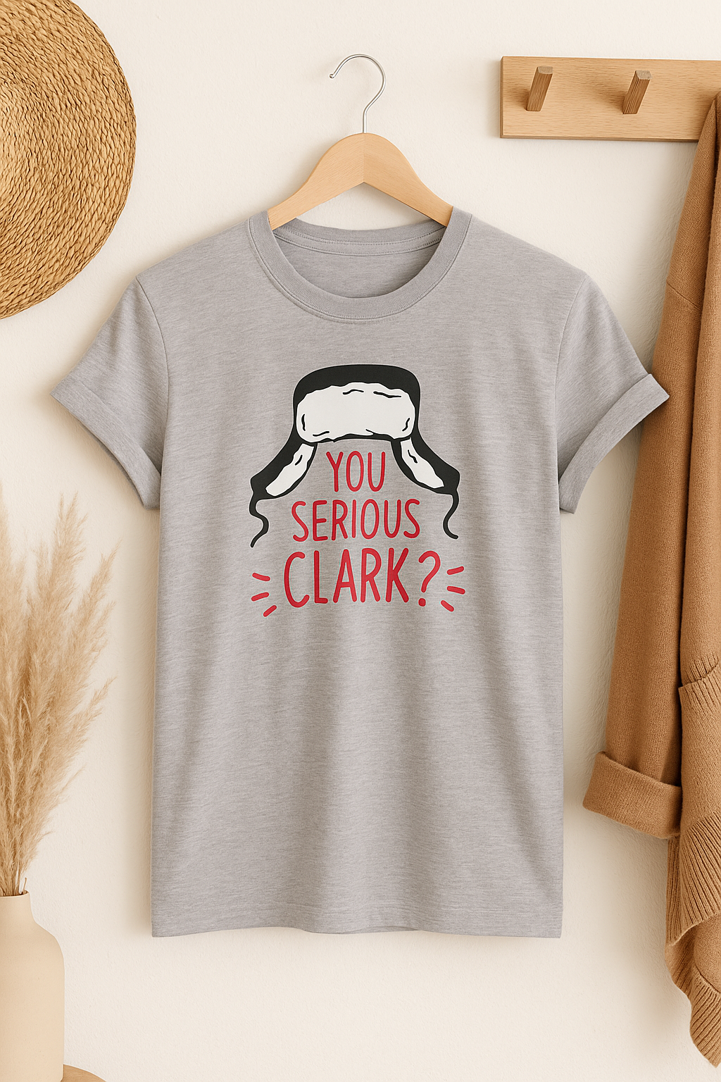 Gray t-shirt with 'You Serious Clark?' graphic on a hanger against a neutral wall.