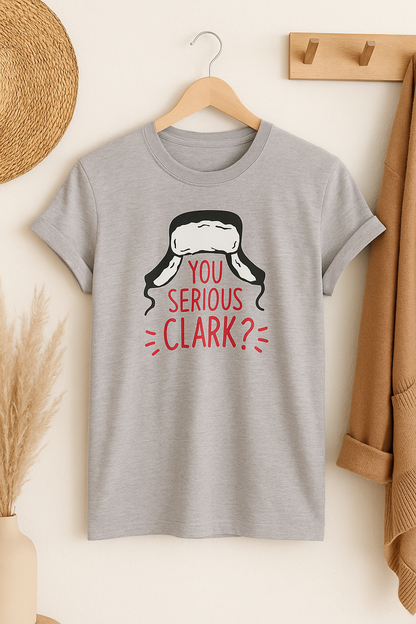 Gray t-shirt with 'You Serious Clark?' graphic on a hanger against a neutral wall.